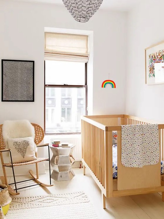a pretty little nursery with a stained crib and chair, some art, neutral and printed textiles, and a metallic side table