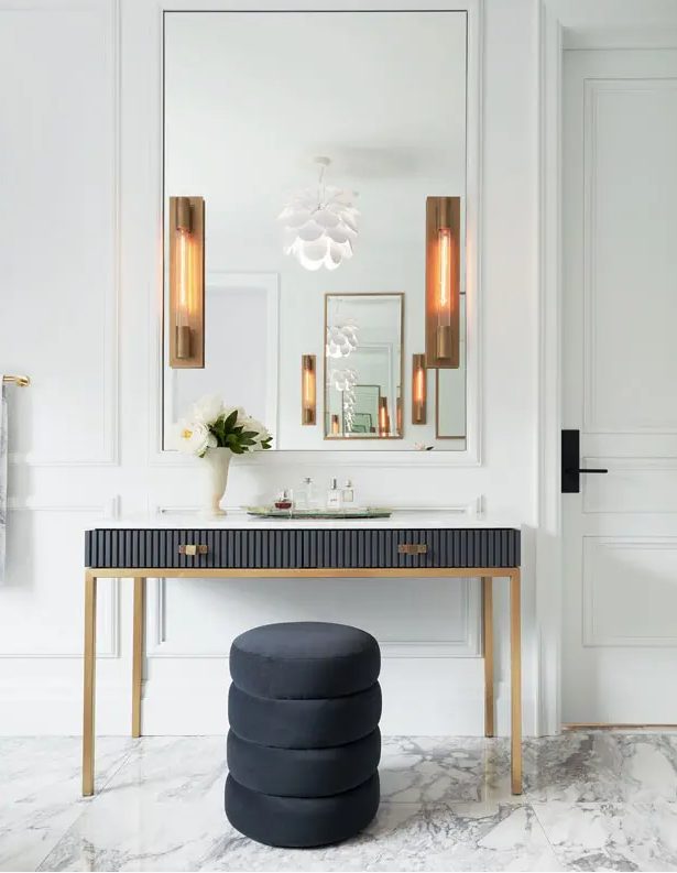 a sophisticated entrance area with a large mirror, a soot vanity with a ribbed surface, a soot stool and chic wall lights