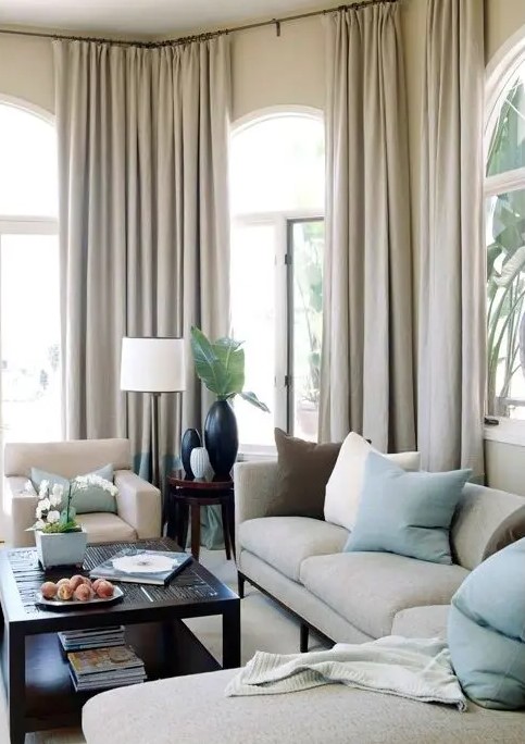 a sophisticated, neutral living room with arched windows draped in neutral curtains, a sitting area with neutral and mint pillows, and a dark coffee table for contrast