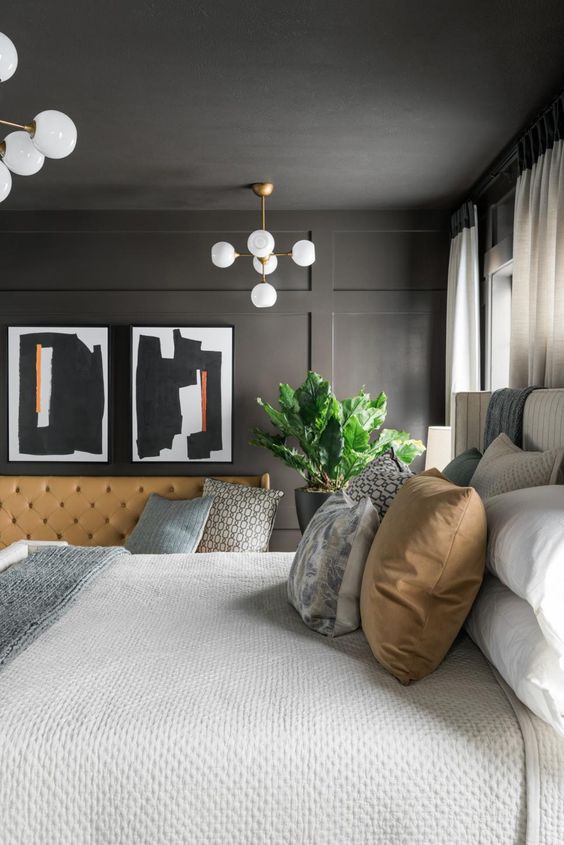 a sophisticated soot bedroom with paneling, a bed with neutral linens, some artwork and a beige leather sofa