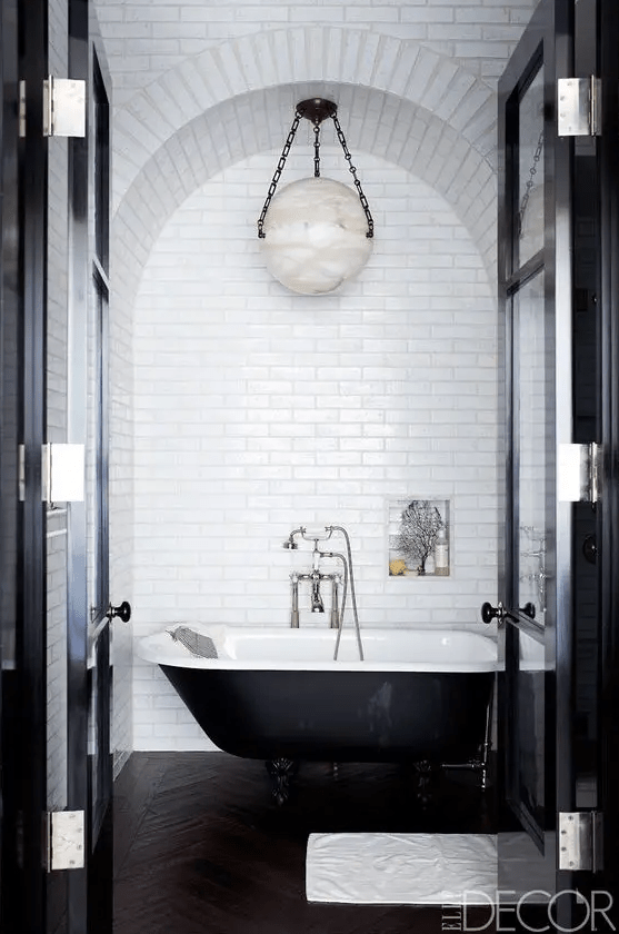 a black and white retro bathroom with white subway tiles, a black clawfoot tub, a hanging lamp and a niche for storage