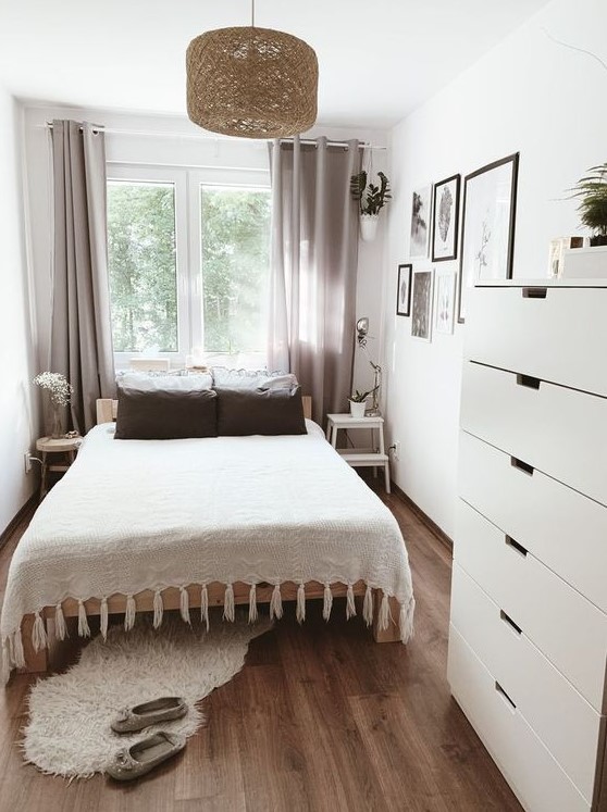 a simple and stylish small bedroom with a bed, mismatched bedside tables, a dresser, a woven hanging lamp and gray curtains