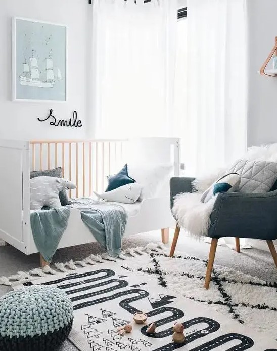 a small Scandinavian children's room with a white cot, a gray chair, pastel pillows and textiles, some artwork and layered rugs and stools
