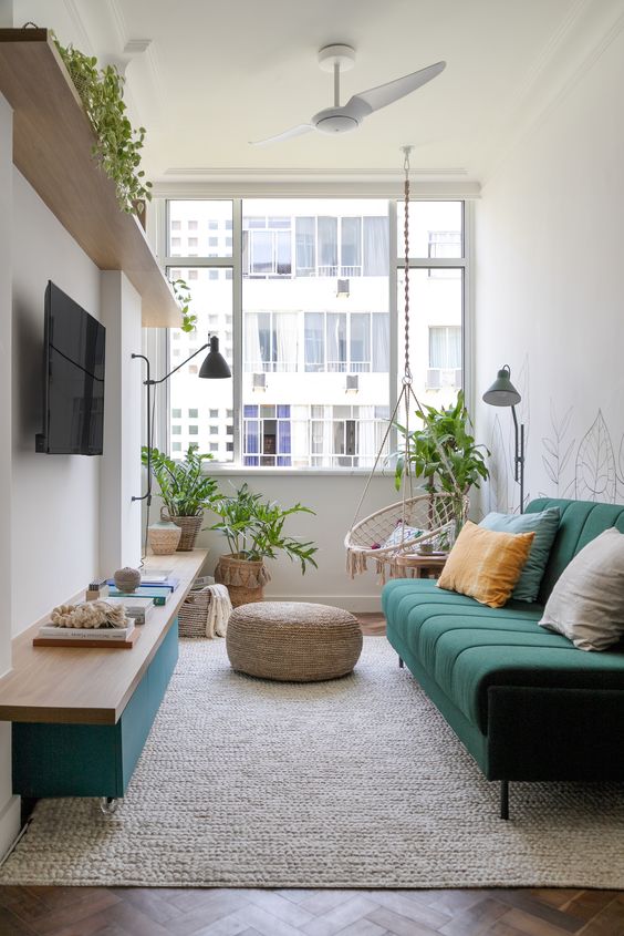 a small and bright living room with an open shelf, a green TV, a green sofa, some potted plants, a chair and lamps