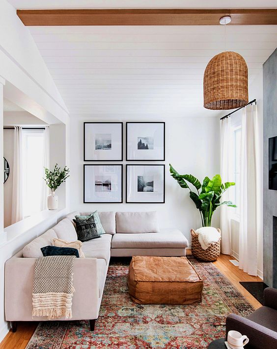 a small and chic living room with a blush sofa, a gallery wall, a printed rug, a leather ottoman and a woven pendant lamp