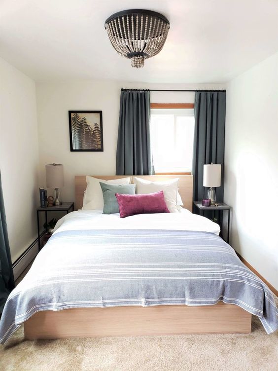 a small and narrow bedroom with a light stained bed and neutral linens, bedside tables with lamps and a beaded chandelier