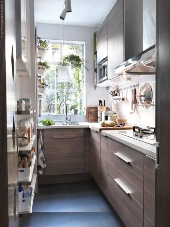 a small and narrow galley kitchen with white stone countertops, herb pots and some open shelves