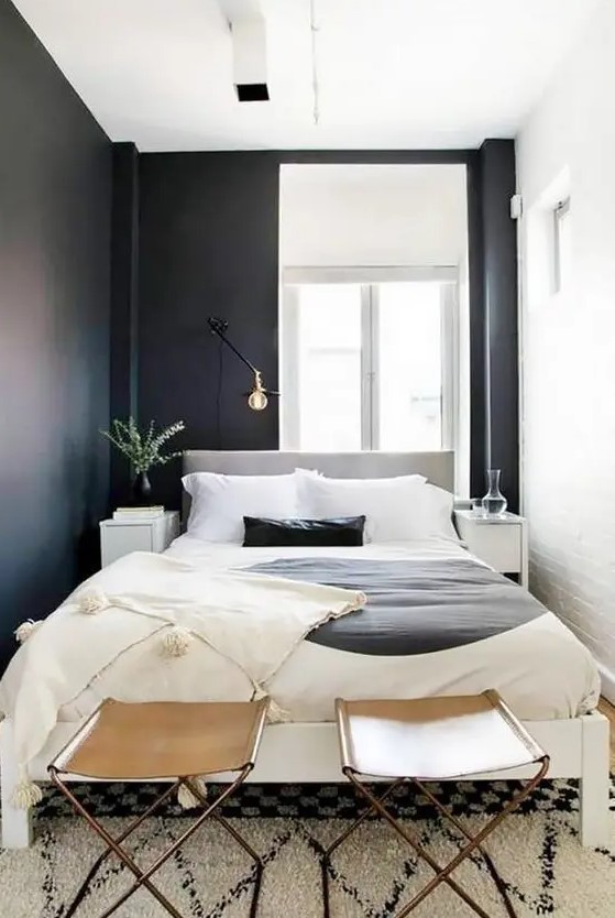 a small and narrow modern bedroom with black and white walls, a neutral bed with statement bedding and leather stools