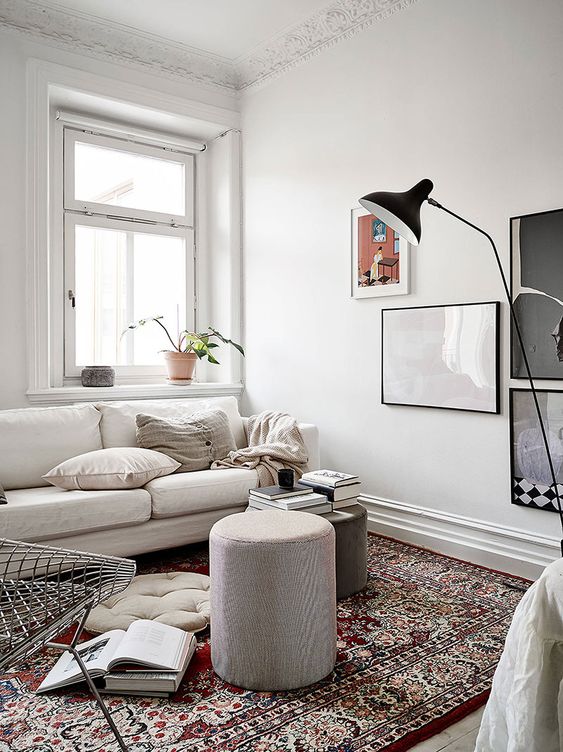 a small and inviting living room with a neutral sofa, a few stools, a chair, a gallery wall and a printed rug