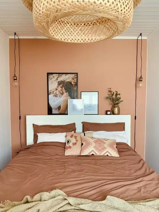 a small bedroom with a terracotta accent wall, a white bed and terracotta linens, and a large woven lamp