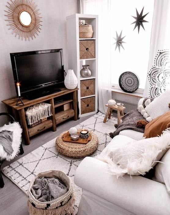 A small boho living room in neutral tones with a white sofa, woven fabrics, a wooden TV, stars and a sunray mirror on the wall