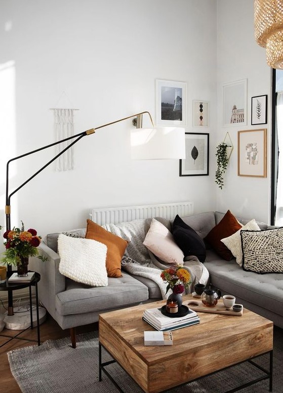 A small modern living room in boho style with a gray sofa, a wooden table, a gallery wall, a floor lamp and light pillows