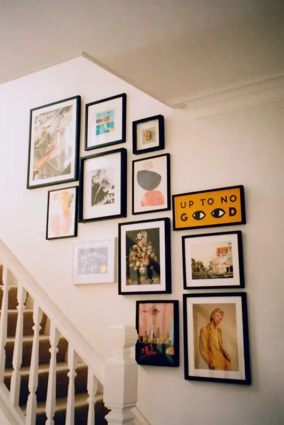 A small gallery wall with mismatched black frames and pretty, bright artwork and other things is a cool idea to utilize the space above the stairs