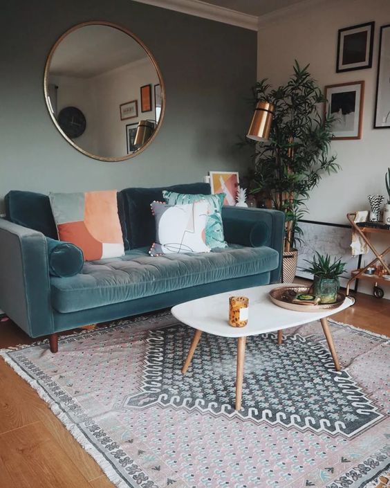 a small living room with a green accent wall, a blue sofa with printed pillows, a printed rug, a coffee table, a bar cart and green plants