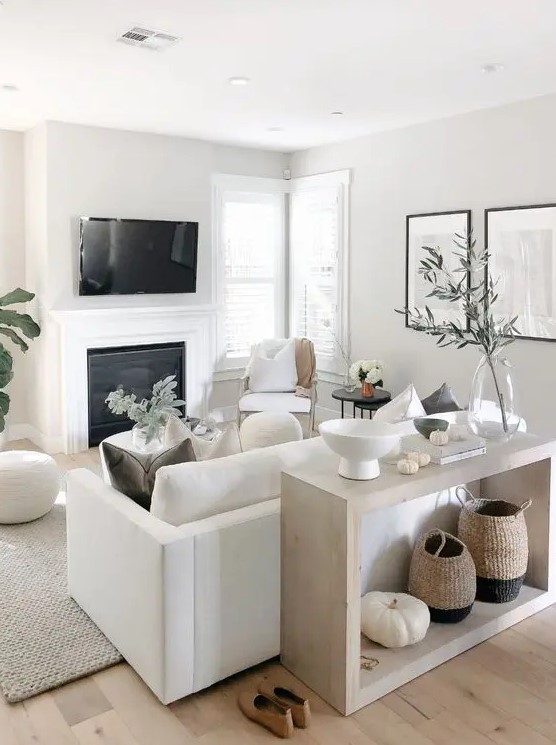 a small neutral living space with a white sofa and chairs, a built-in fireplace, a console and some accessories and green plants to freshen up the space