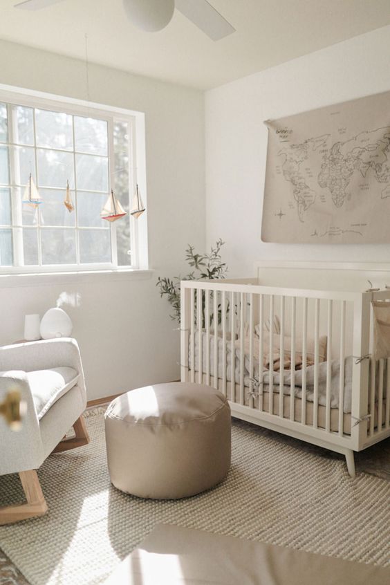 A small, neutral nursery with a crib, rocking chair, gray stool, layered rugs, and some pretty decor is very inviting