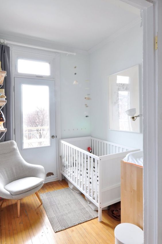 a small neutral nursery with a white crib, changing table, neutral chair, some bookshelves and neutral decor