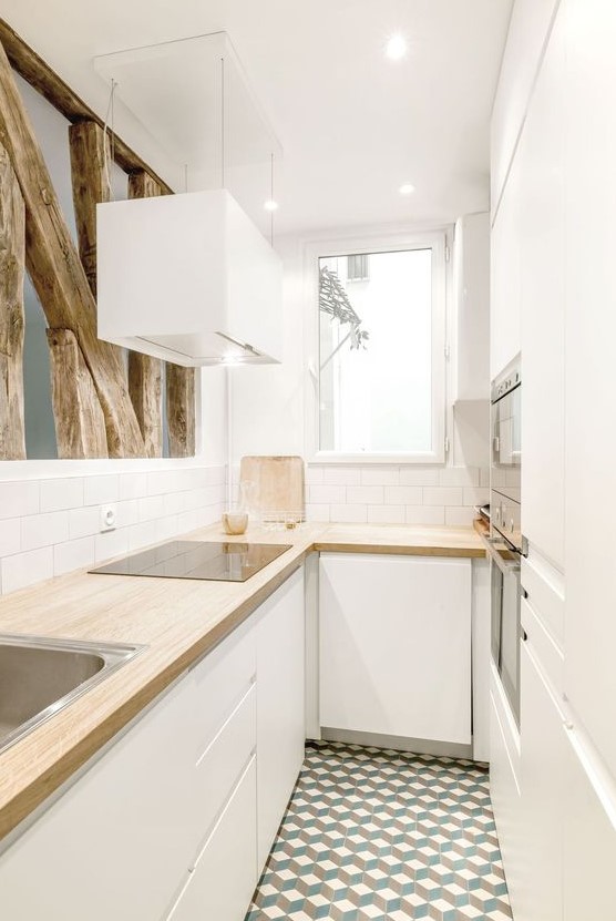 a small white minimalist U-shaped kitchen with butcher block countertops, white subway tiles and raw wood for decoration