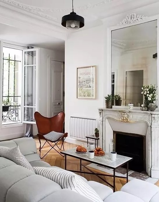 a small but chic French-style living room with an antique fireplace, a coffee table, a brown butterfly chair and a gray sofa