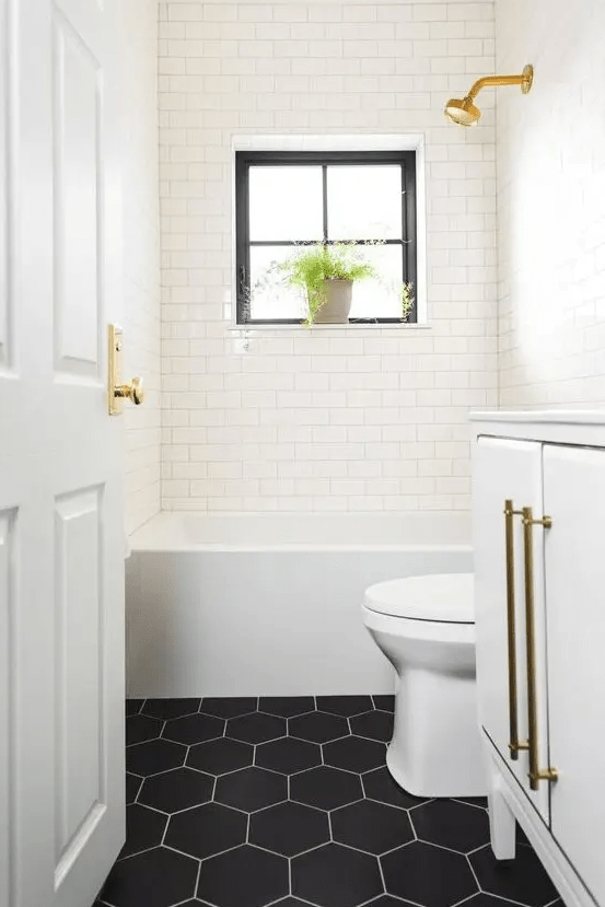 A small but cool bathroom with white subway tiles and black hexagon tiles, gold accents and potted plants is a beautiful space