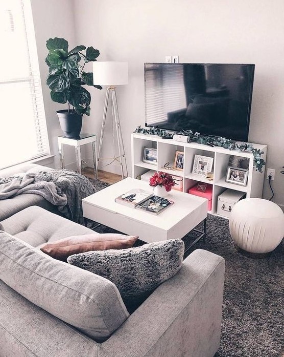 a small but cozy living room with a small gray sofa, a TV, a white table and some lamps as well as a potted plant