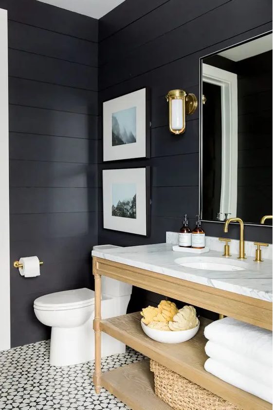 A sooty bathroom with a light stained vanity and baskets, a mirror, sconces and a small gallery wall is cool
