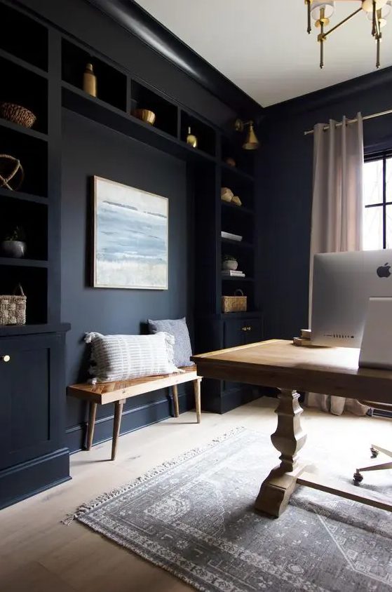 a sooty home office with built-in cabinets and shelves, a light-stained vintage table, bench and a printed rug