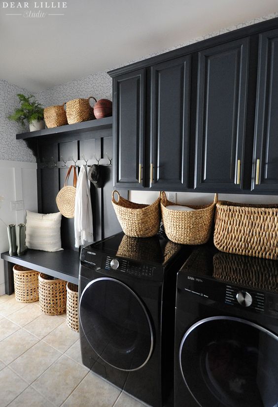 A soot laundry room with a shelf and bench, baskets for storage, and black appliances is a cool and chic space