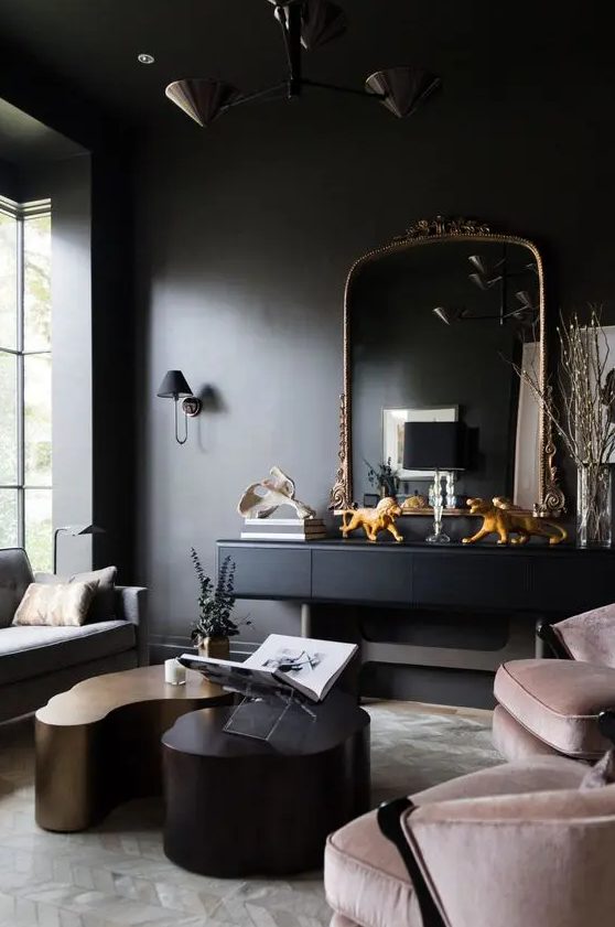 a sooty living room with a black console and chic mirror, pink chairs, a gray sofa and statement coffee tables