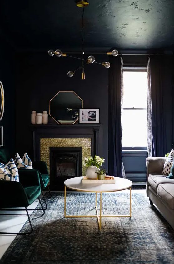 a sooty living room with a gold and soot paneled fireplace, a neutral sofa, a coffee table, green chairs and a stylish chandelier