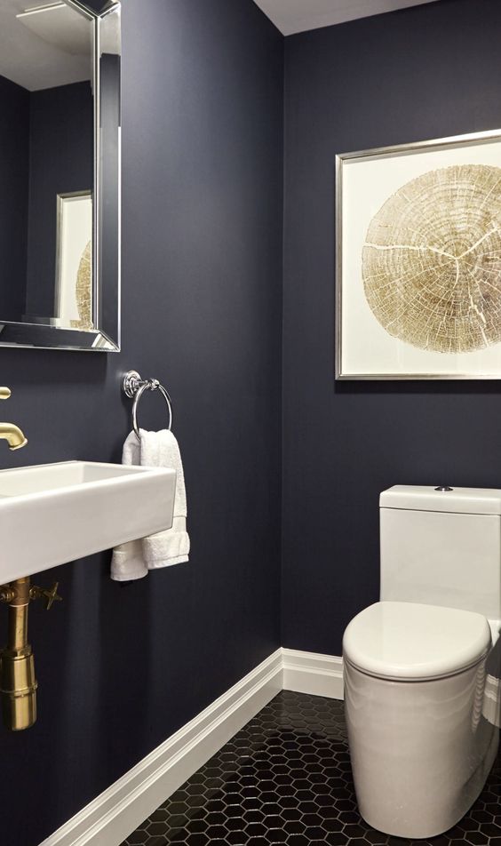 A soot toilet with white appliances, a piece of art, gold fixtures and a glamorous mirror is a cool and chic space