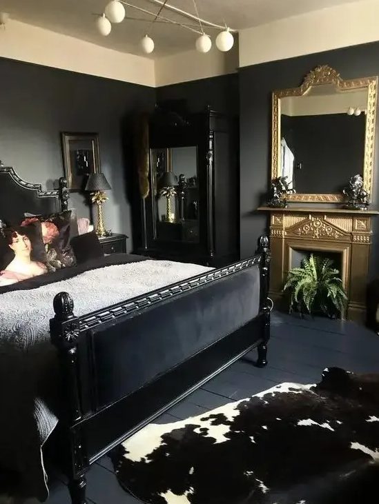 an elegant bedroom with black walls, a black bed and mirror, a gold fireplace and mirror, and some plants and artwork