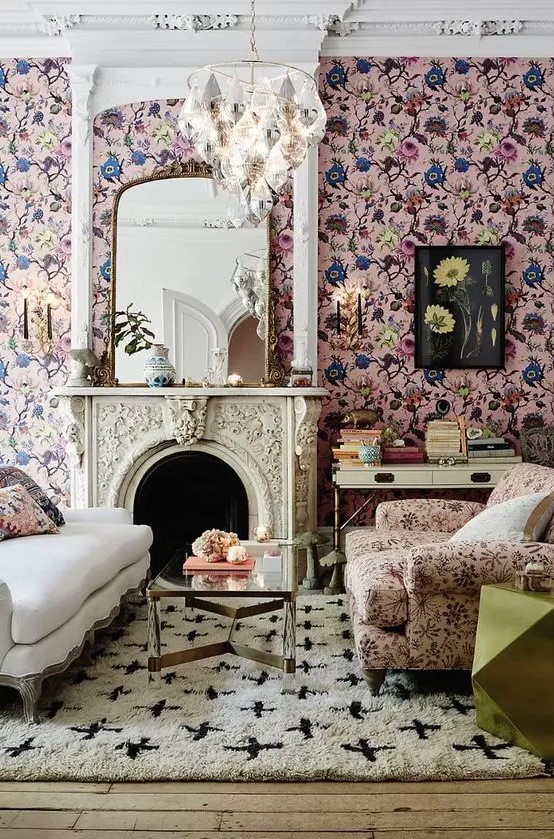 an elegant living room with pink floral wallpaper, a cream sofa, a pink floral chair, a coffee table, a fireplace and a chandelier