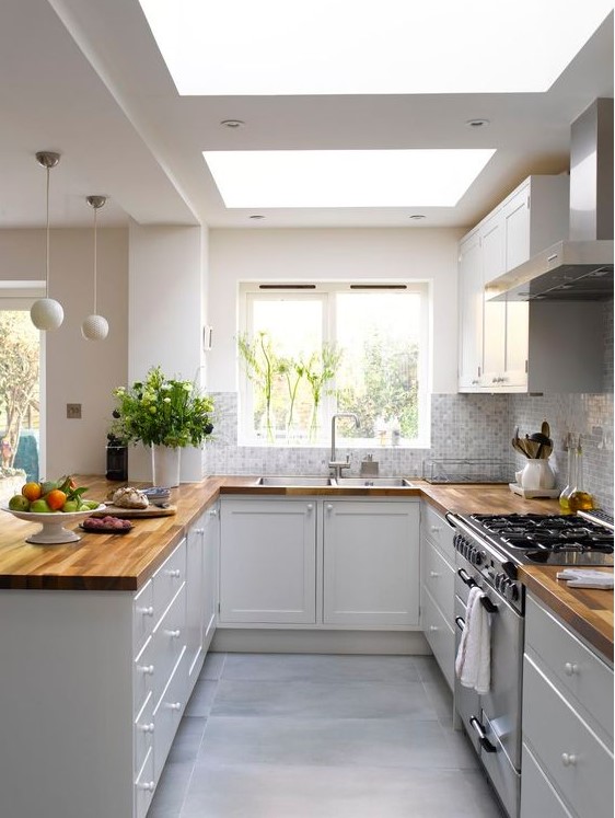 a stylish U-shaped kitchen in white, with only butcher block base cabinets and countertops, skylights and hanging globe lamps