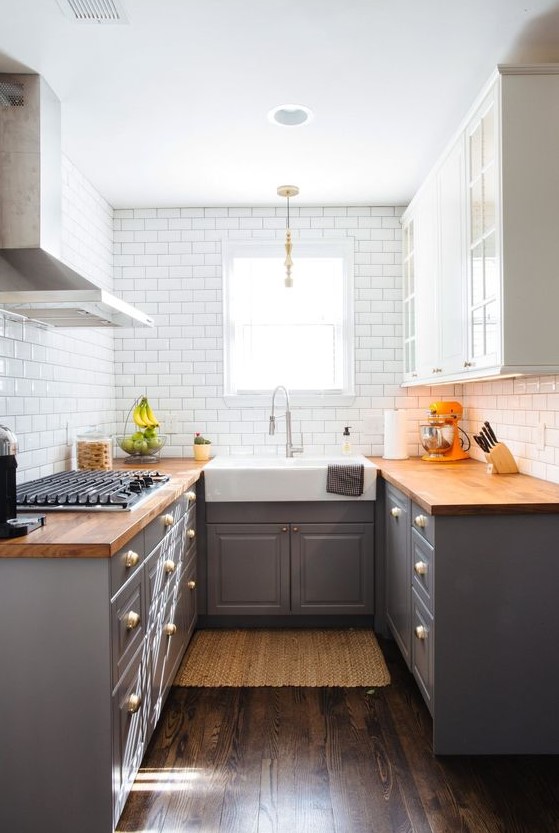 A stylish mid-century modern kitchen with gray base cabinets and white upper cabinets, butcher block countertops and white subway tiles