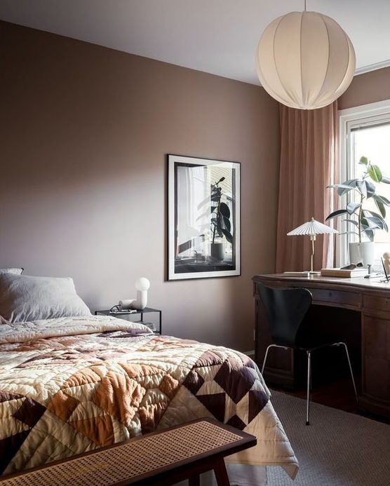 A stylish modern brown bedroom with a bed and printed linens, a dark stained desk and a black chair
