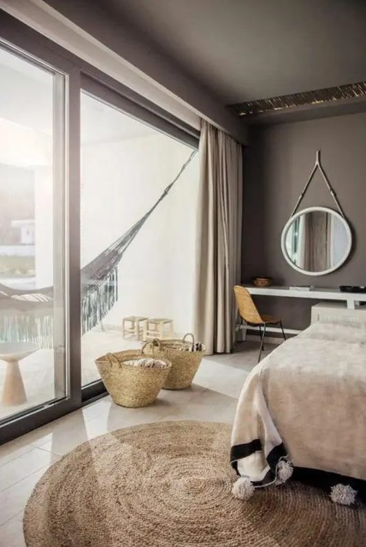 a taupe bedroom with an upholstered bed, a console that doubles as a vanity, a round mirror and a hammock on the balcony