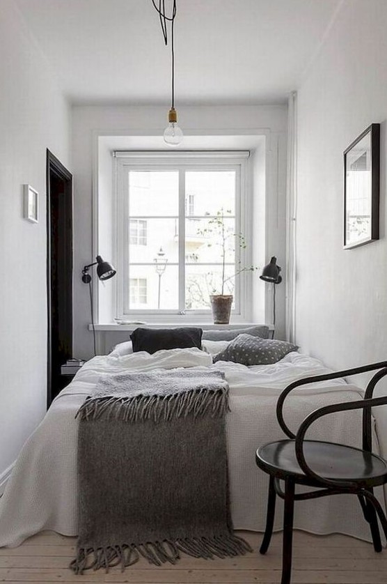 a small Scandinavian bedroom with black wall lamps, a black chair and a bed with comfortable linens
