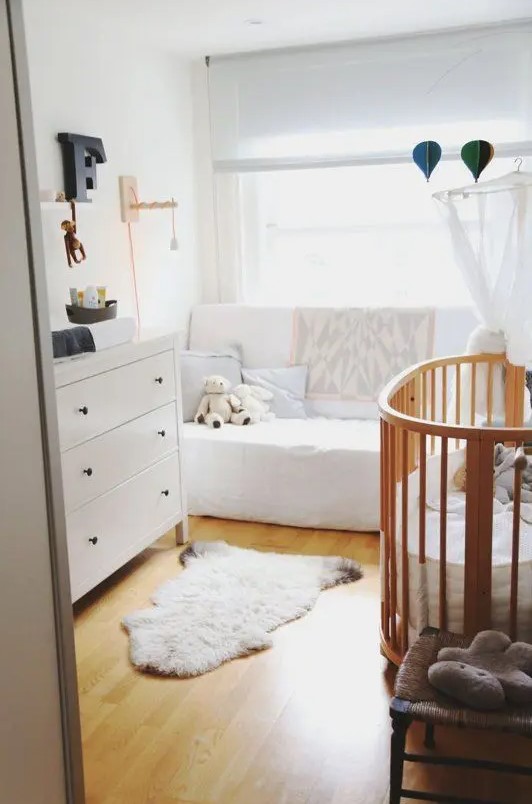 A small and cozy mid-century modern nursery with a white dresser, white sofa, stained crib, shelves, rugs and neutral curtains