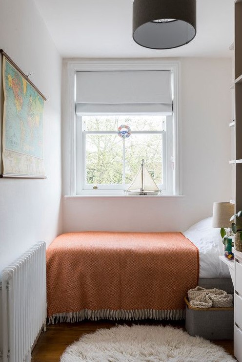 A small bedroom with a bed with a rust blanket, a box of blankets, a shelf and some decorations is suitable as a guest room or even a children's room