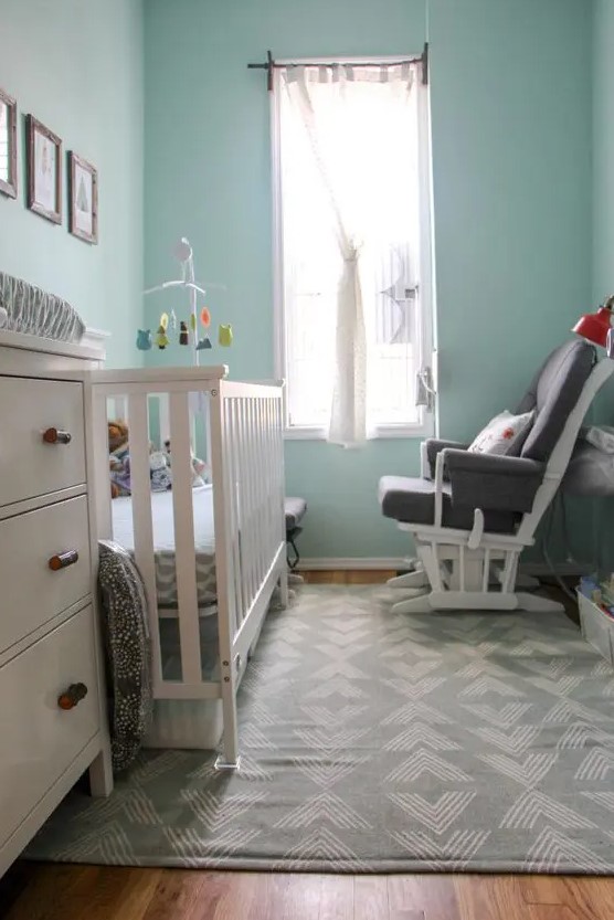 a small modern children's room with light blue walls, a white cot and chest of drawers, a gray chair, a gallery wall and printed textiles