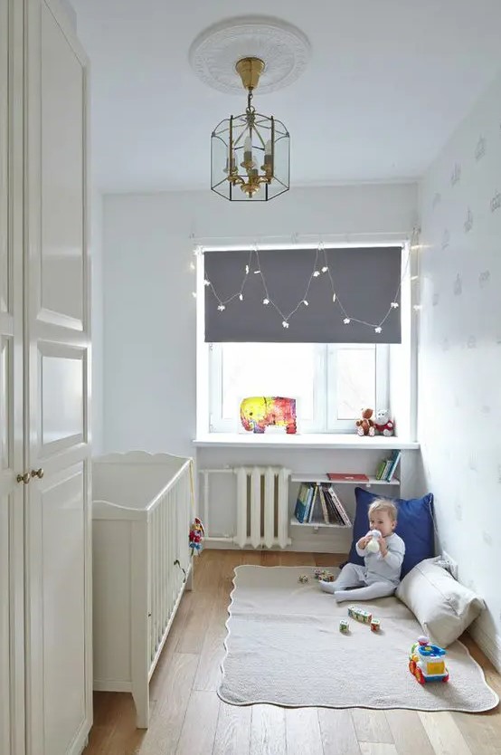 a small children's room with a white vintage cot, a windowsill as a table, some bookshelves and a play area on the floor