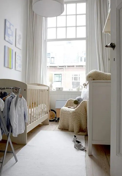 a small white nursery with a neutral crib, white dresser, neutral chair, makeshift closet and some art and toys