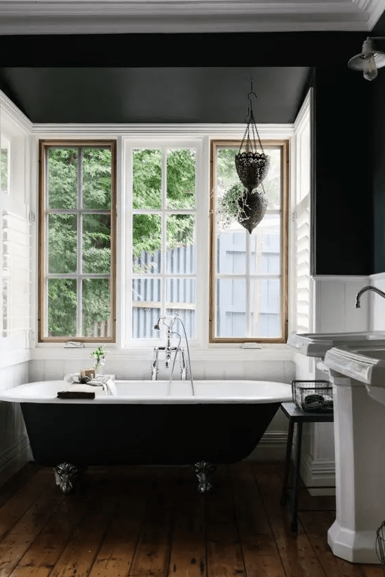 a vintage bathroom with black walls and white floorboards, a black clawfoot tub, freestanding sinks and a window