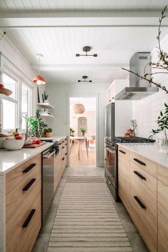 an inviting, brightly stained galley kitchen with white countertops and a tiled backsplash, with potted plants and pendant lamps