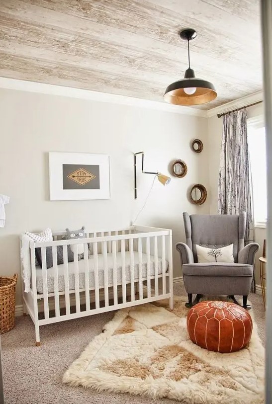 An inviting mid-century modern nursery in neutral tones, featuring a white crib, gray rocking chair, layered rugs, a leather ottoman and some artwork