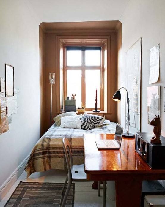 an inviting small bedroom with a bed and printed linens, a stained desk and chair, a table lamp and a gallery wall