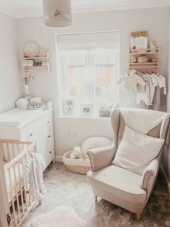 a white nursery with a white dresser, a stained crib, a neutral chair, bookshelves, a makeshift closet and some decorations