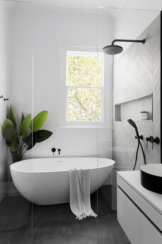 an airy Scandinavian bathroom with gray and white tiles, a floating white vanity, a black sink, a freestanding bathtub and a statement plant