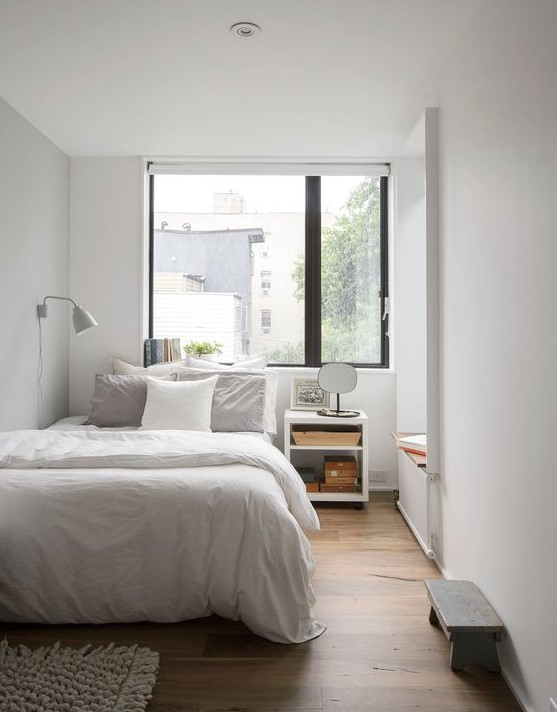 an airy and inviting small white bedroom with white furniture, a small bench, a bedside table and a day bed by the window